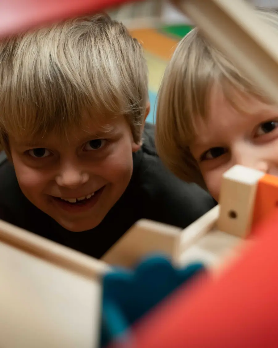 To smilende gutter kikker fram gjennom et dukkehus i klasserommet