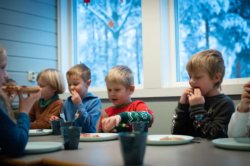 Elever spiser lunsj ved et langbord foran store vinduer med snø ute
