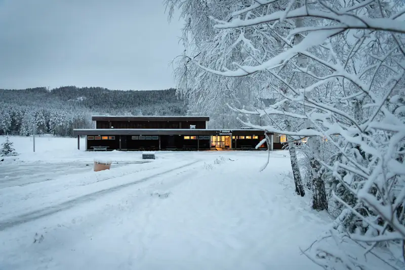 Lisleherad Montessoriskole sett fra veien, med snødekte trær og lys i vinduene