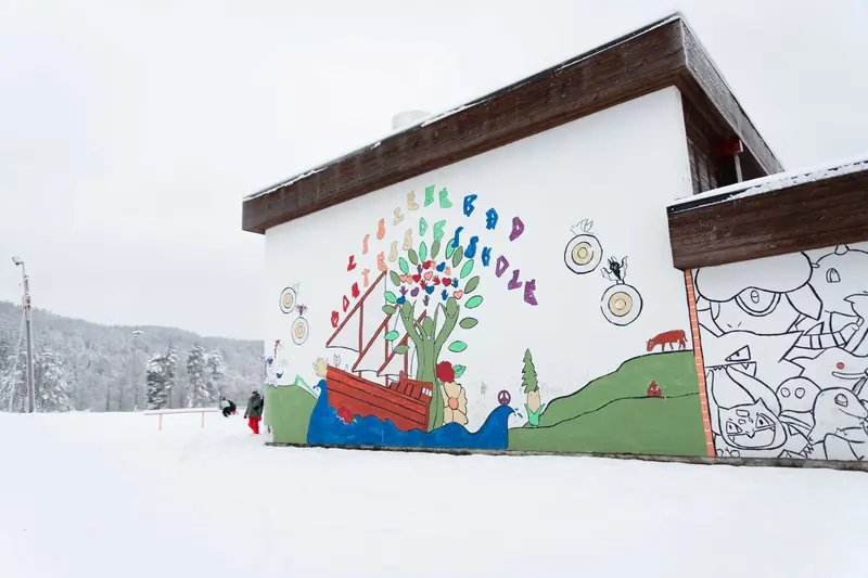 Skolebygget med et fargerikt veggmaleri av et tre og et skip, i snøen